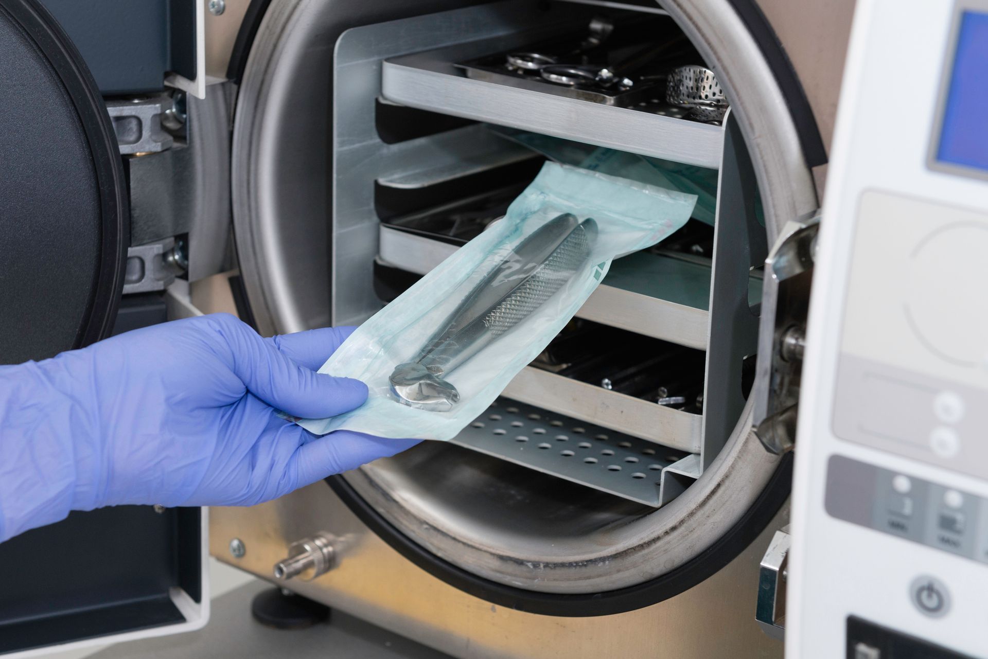 Mano guantata che inserisce una confezione sigillata di strumenti chirurgici in un'autoclave aperta per la sterilizzazione.