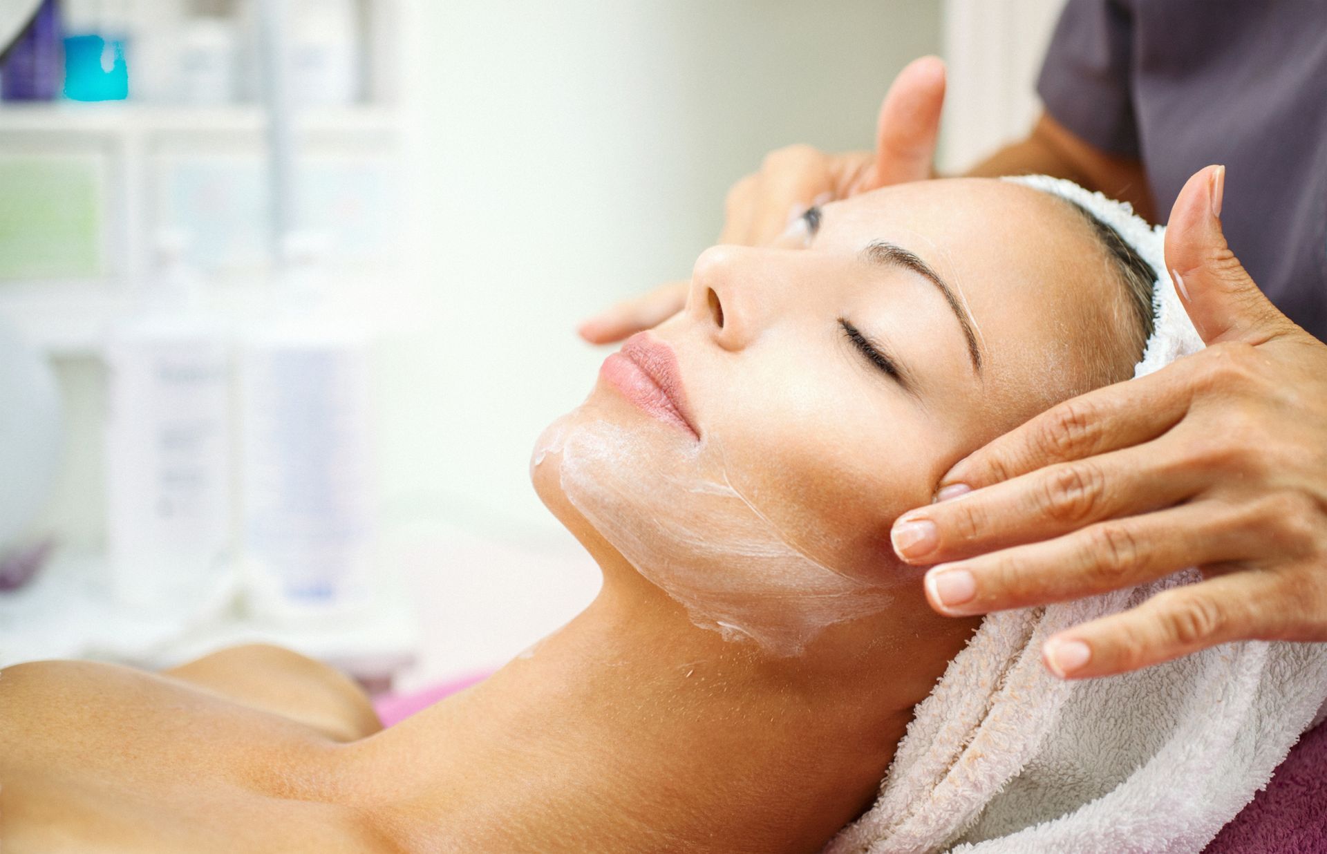 Donna che riceve un massaggio al viso in una spa; mani che applicano la crema sul viso.