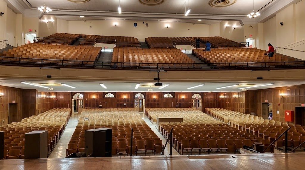 Empty theater auditorium with rows of tan seats and a stage viewed from two angles