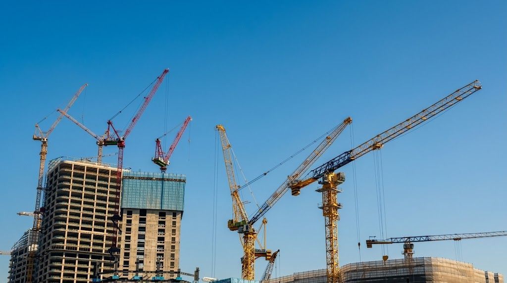 Construction site with multiple cranes and a partly built high-rise against a blue sky
