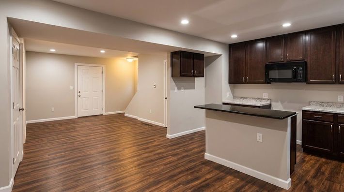 Empty open-concept kitchen and living area with dark wood floors, brown cabinets, and recessed lighting.
