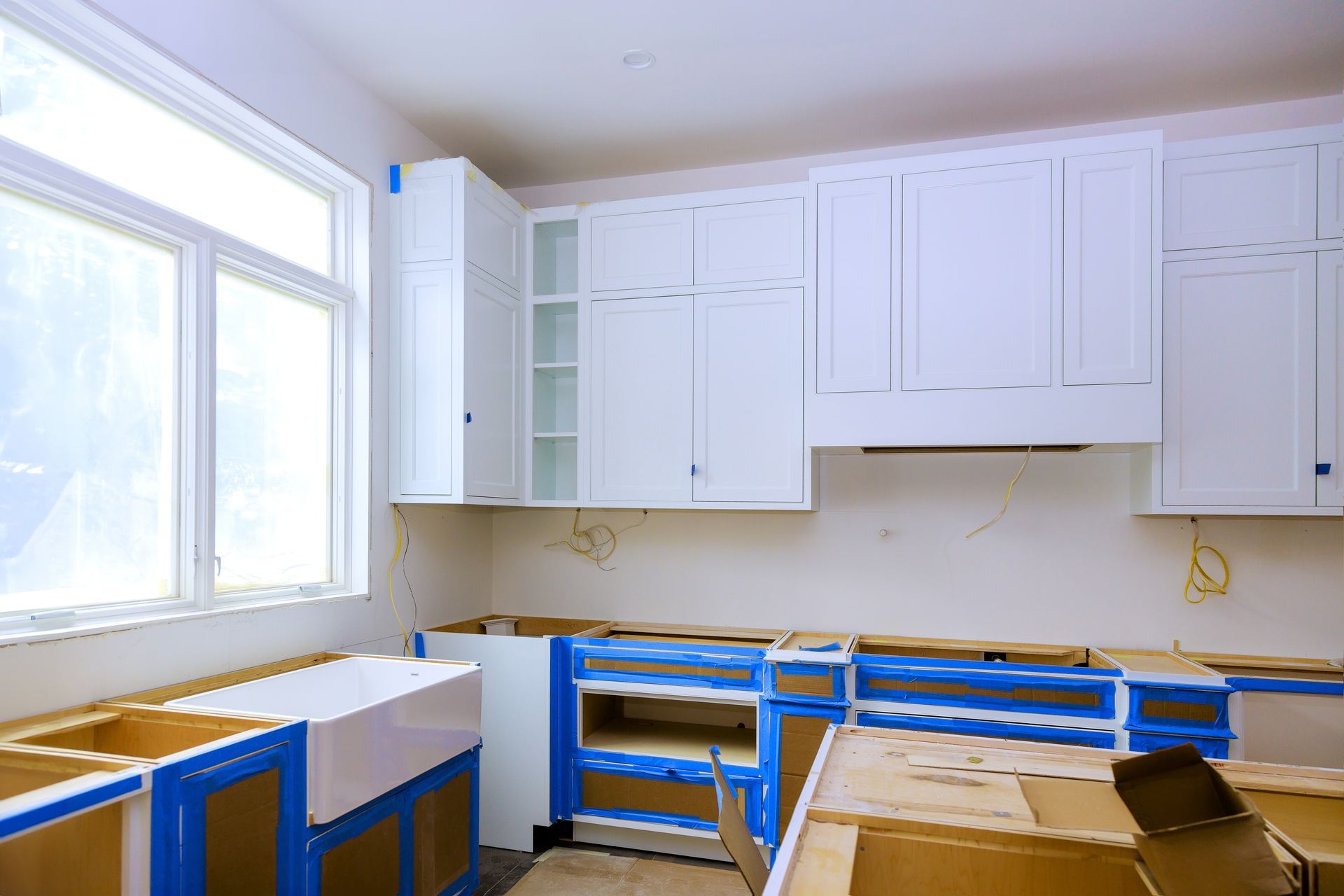 New kitchen construction underway featuring white cabinets with unfinished cabinetry blue masking tape for protection.