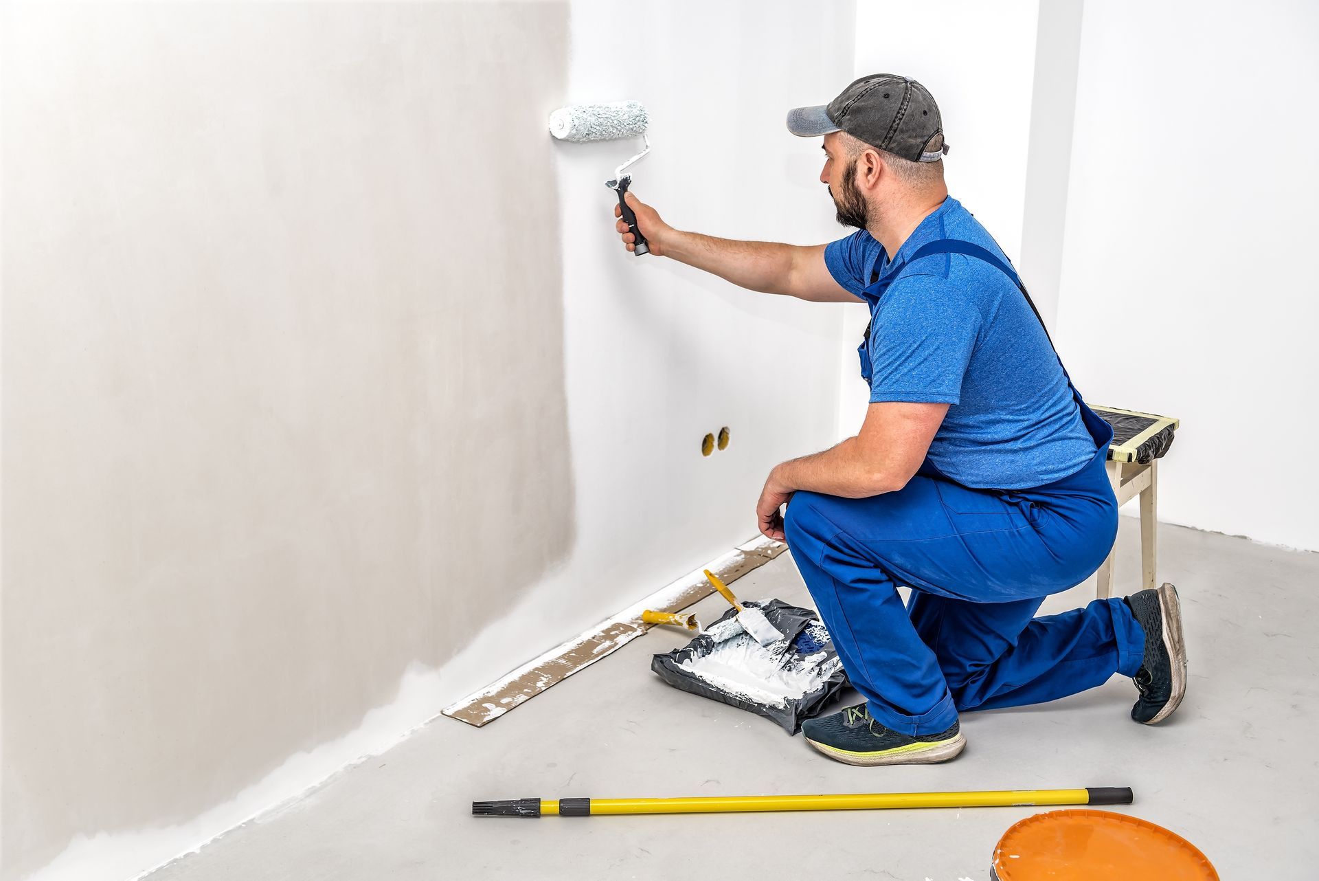 Builder in blue painting the wall with painting roller in white color.
