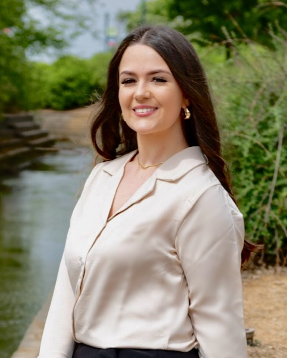 Woman in cream-colored blouse smiles near a body of water in a natural setting. Woman in cream-colored blouse smiles near a body of water in a natural setting.