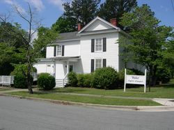 A two-story, white, historic-style building with black shutters and a sign that reads 