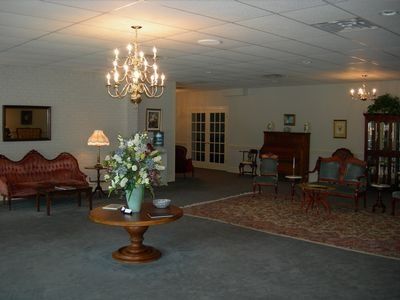 A spacious, traditional lounge with a chandelier, upholstered furniture, a round wooden table with flowers, and area rugs.