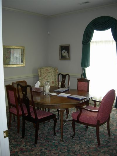 Dining table with six chairs, featuring pink upholstery, in a room with a large window and green arched curtains.