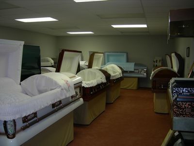 An indoor showroom featuring several open caskets of various colors and materials lined up on stands.
