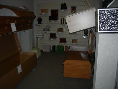 A funeral home showroom featuring wooden coffins and various urns displayed on wall shelves.