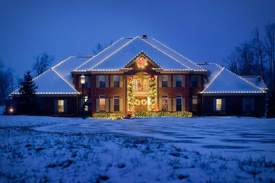 A large brick house with christmas lights on it is covered in snow.
