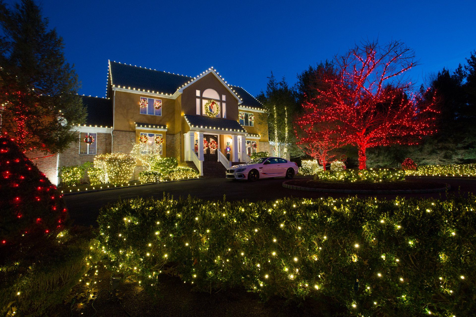 A white car is parked in front of a house decorated for christmas