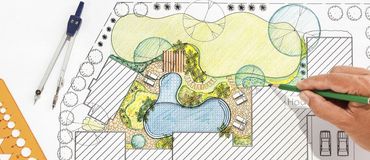 A person is drawing a garden plan with a pencil.
