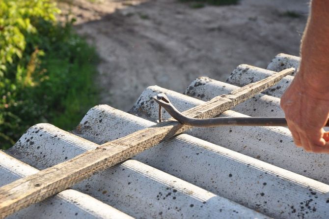 Hand tying rope around white corrugated roofing sheets outdoors