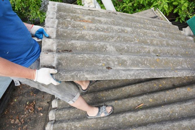 Person lifting a corrugated roof panel during removal on a rooftop