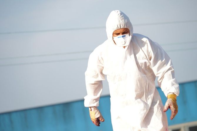 Person in white protective suit and hood standing outdoors near a blue wall
