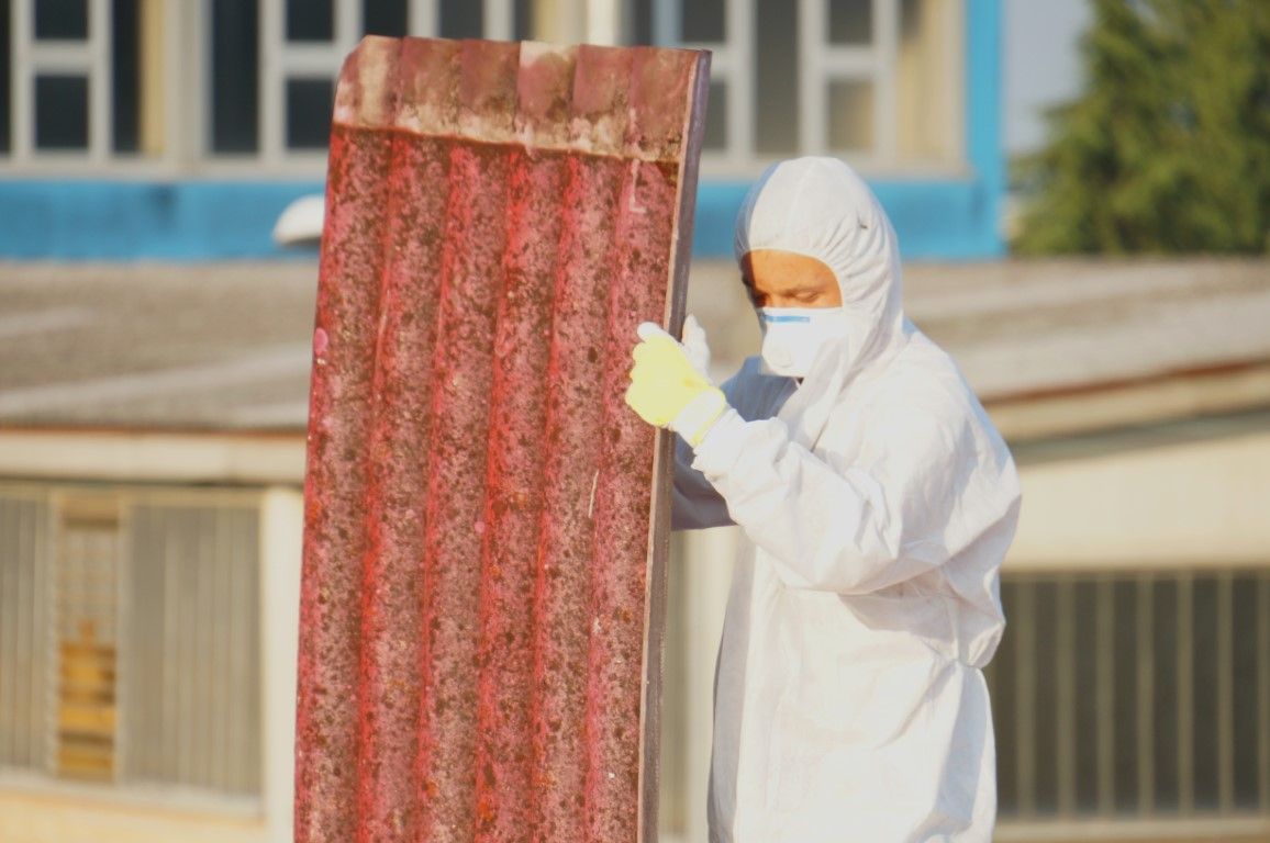 Worker in white protective suit inspecting a rusted metal panel outdoors.