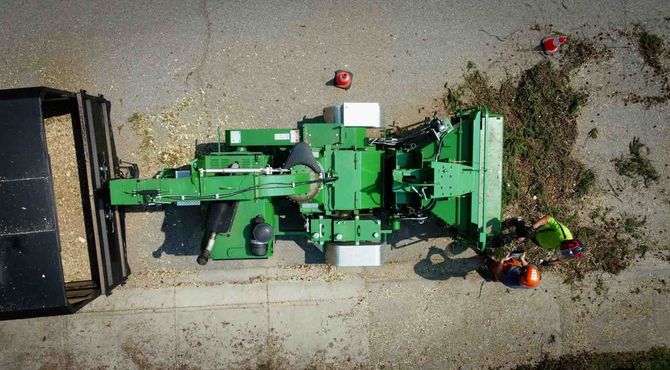 Top-down view of a green farm machine on gravel beside a black truck bed and scattered tools