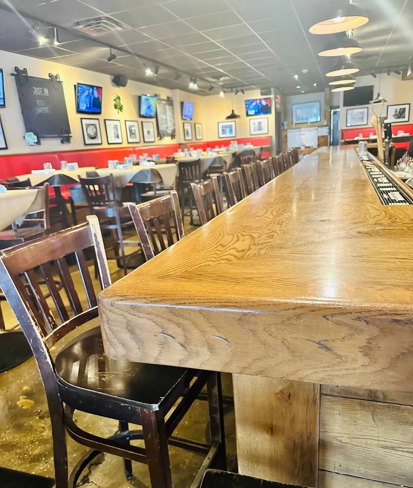 Interior of a quiet bar featuring a long, polished wooden counter and rows of chairs and booths in a softly lit space.