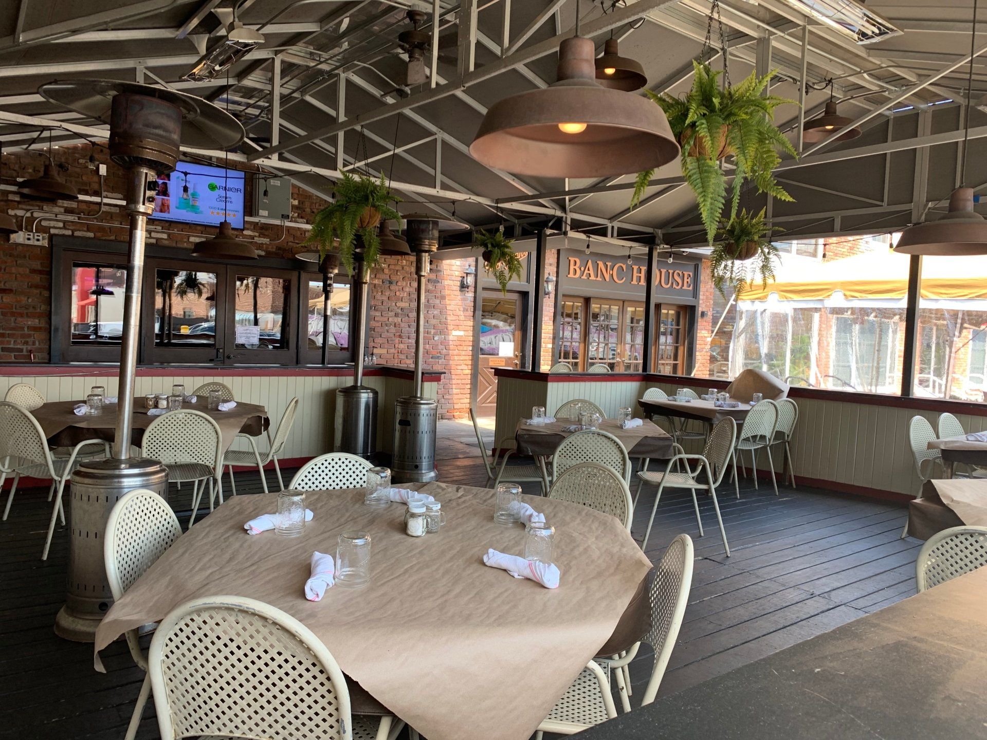 Outdoor restaurant patio with tables, chairs, and hanging pendant lights, featuring brick walls and warm, ambient lighting.