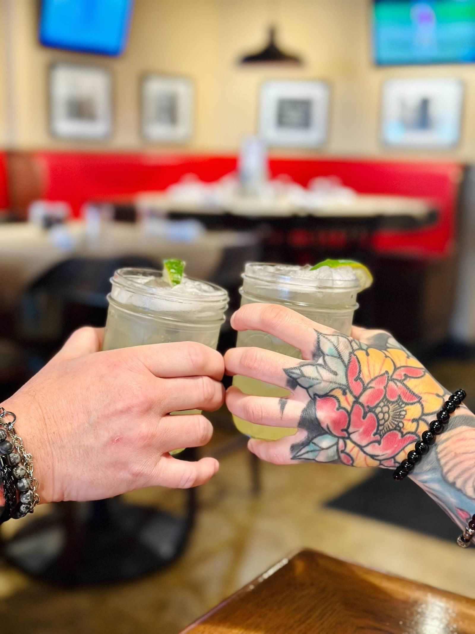 Two hands holding mason jar cocktails together in a toast at a restaurant.