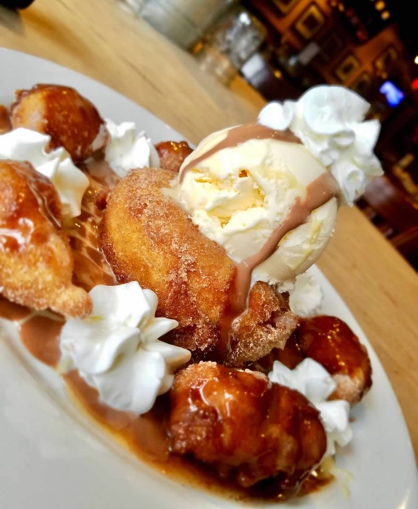 A plate of fried, cinnamon-coated dough balls topped with a scoop of vanilla ice cream, chocolate sauce, and whipped cream.