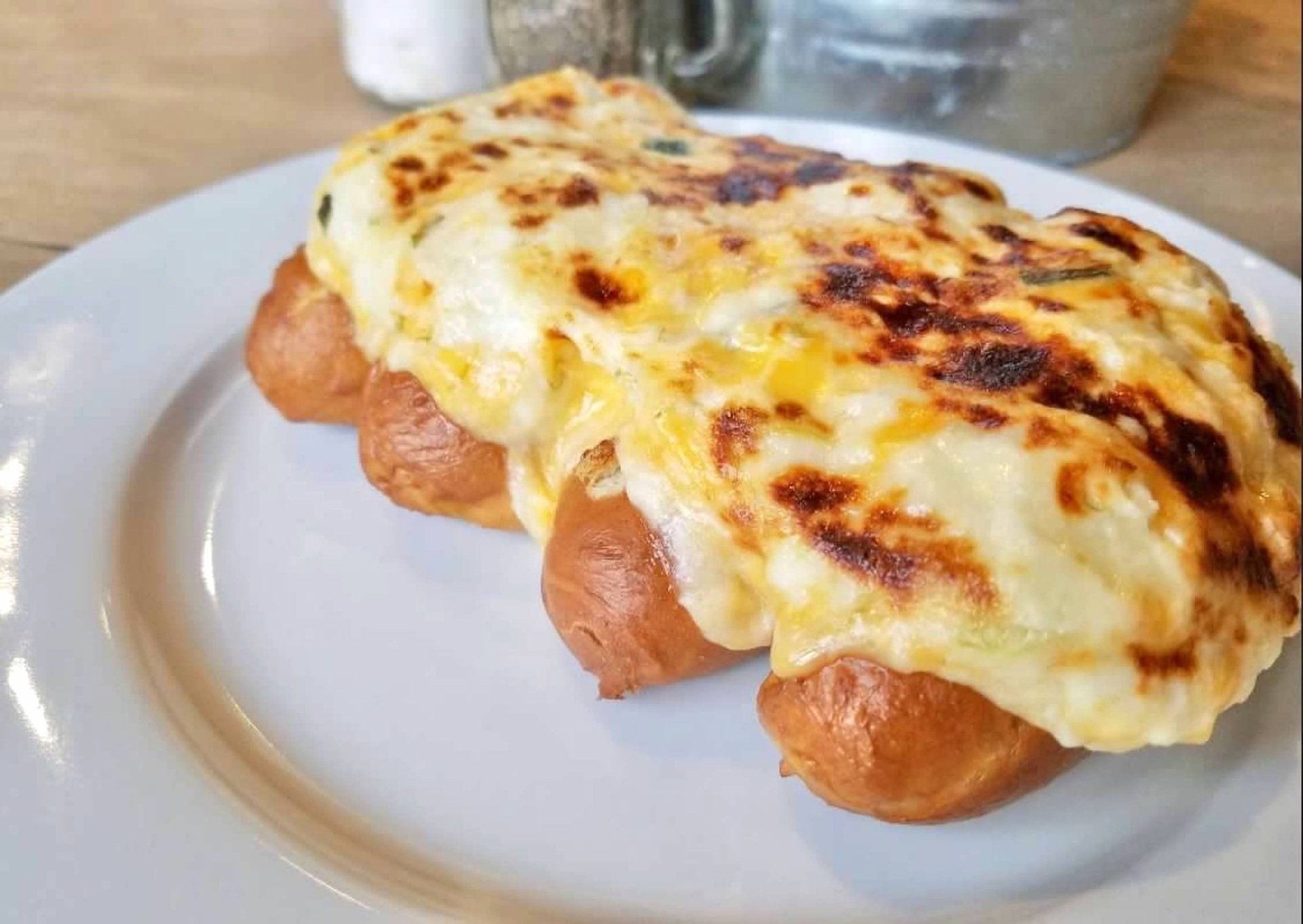 A close-up of sausages topped with melted, browned cheese on a white plate.