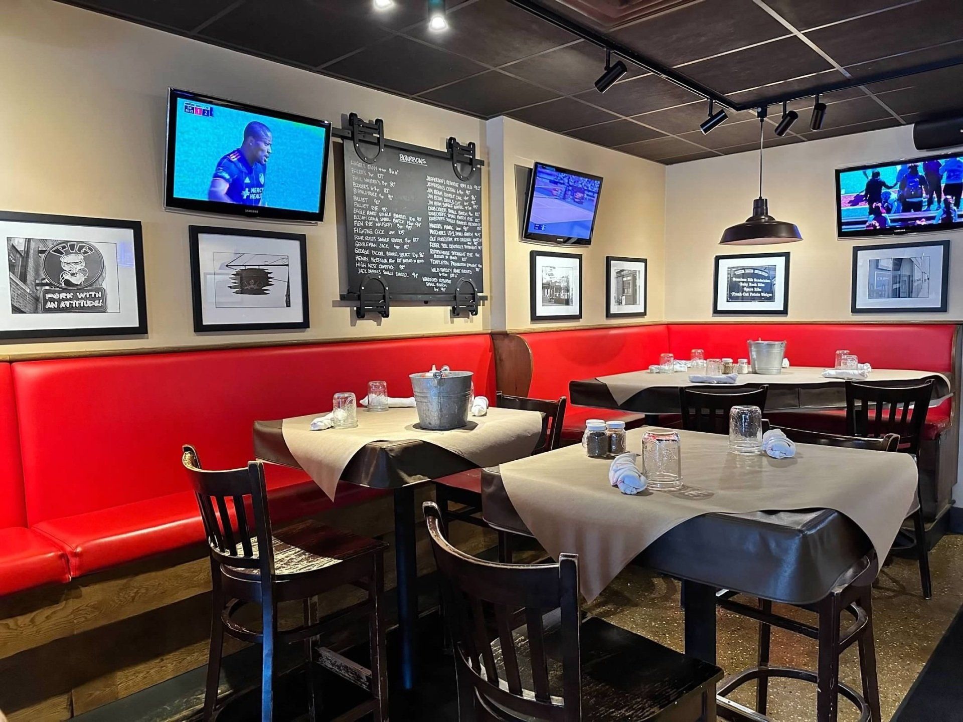 Dining area featuring red booths, tables with tan cloths, framed photos, and TVs on beige walls.