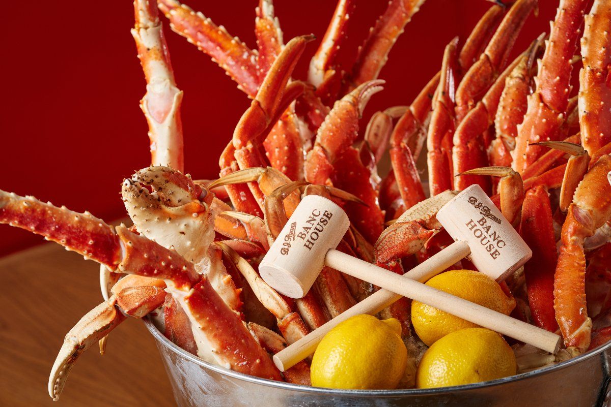 A metal bucket filled with cooked crab legs and fresh lemons, topped with two small wooden mallets.
