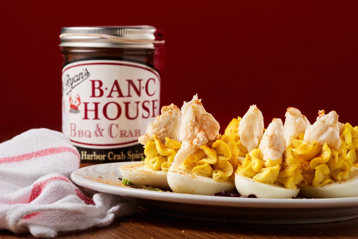 Deviled eggs topped with crab meat on a plate next to a jar of Ryan's B-ANC House Bbq & Crab sauce.
