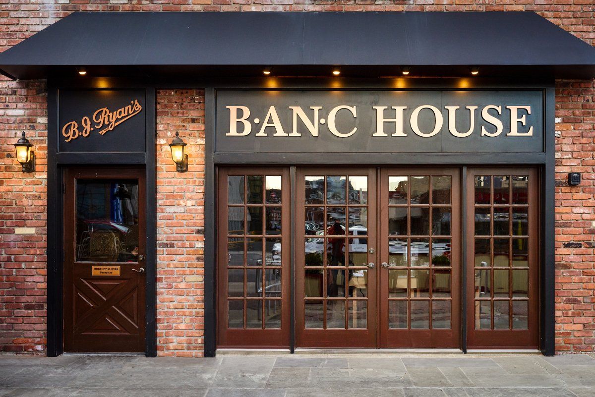 The brick storefront of B.J. Ryan's Banc House, featuring a dark awning and glass double doors.
