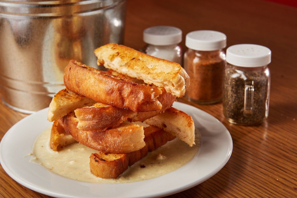 Golden-brown French toast sticks stacked on a white plate with a side of cream sauce, accompanied by three spice jars.