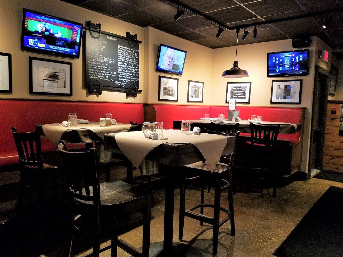 Indoor dining area featuring tables with beige cloths, red bench seating, hanging lights, and televisions on the walls.