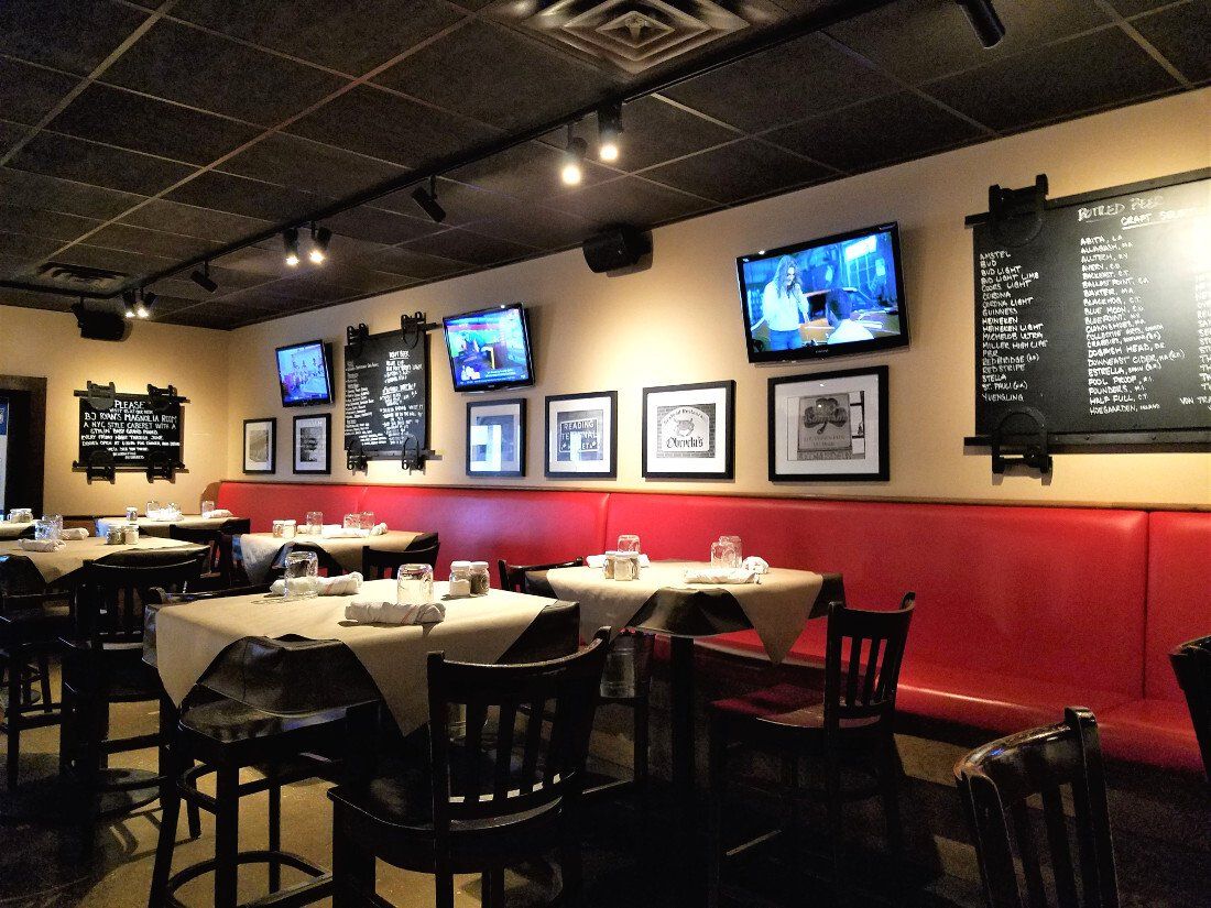 Interior with tables set for dining, red booth seating, wall-mounted TVs, and menu boards on a beige wall.