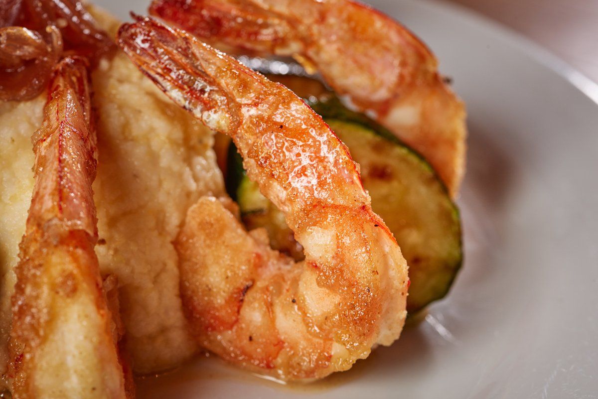 Golden-brown fried shrimp served on a white plate with mashed potatoes and a slice of roasted zucchini.