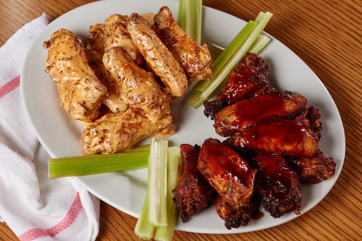 A white platter holds one side of creamy, seasoned chicken wings and one side of dark red glazed wings with celery stalks.