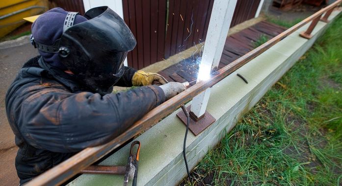 A man wearing a welding mask is welding a railing.
