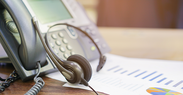 Desk phone headset beside a smartphone on a table with charts in the background
