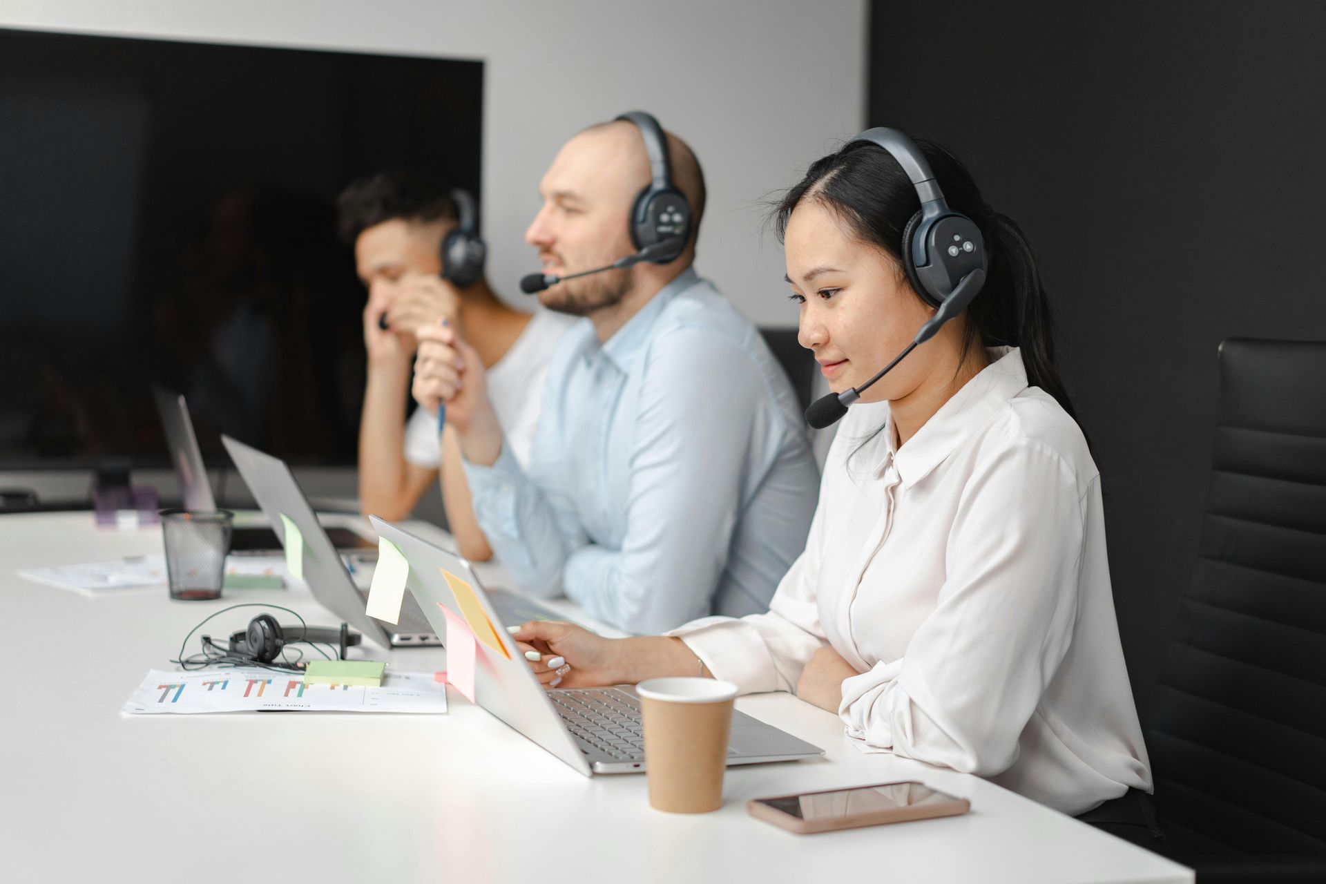 Three headset-wearing call center agents working at laptops in a modern office