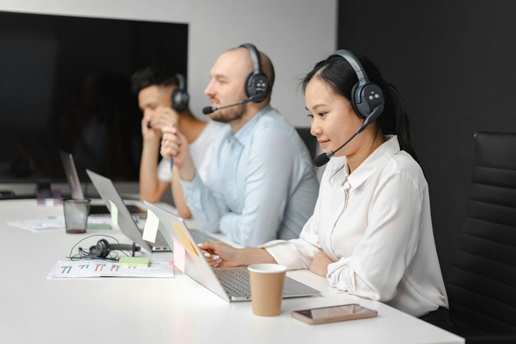 Three headset-wearing call center agents working at laptops in a modern office