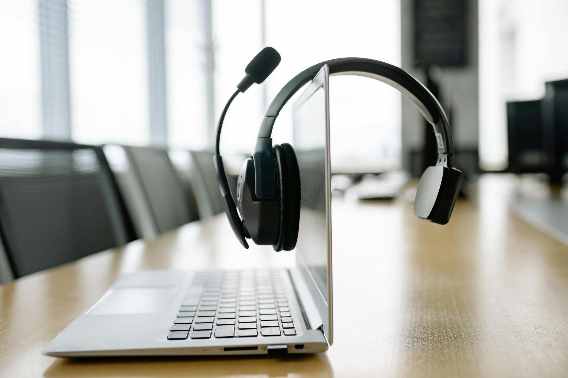 Laptop with headset on a conference table in a bright office meeting room