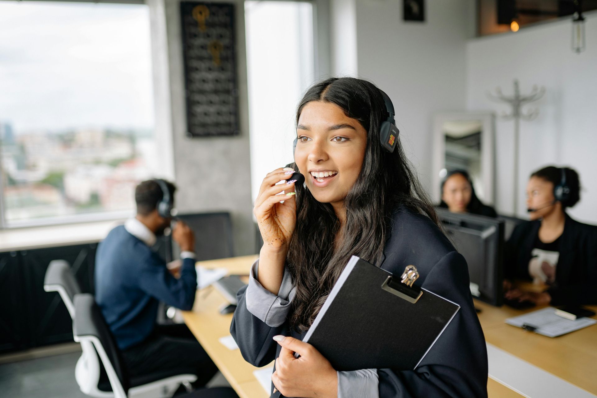 Office team meeting with a smiling presenter holding a notebook and speaking on a headset