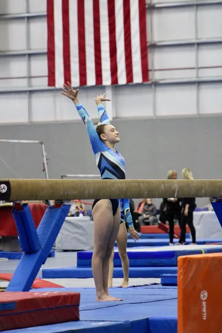 a female gymnast is standing on a balance beam in front of an american flag