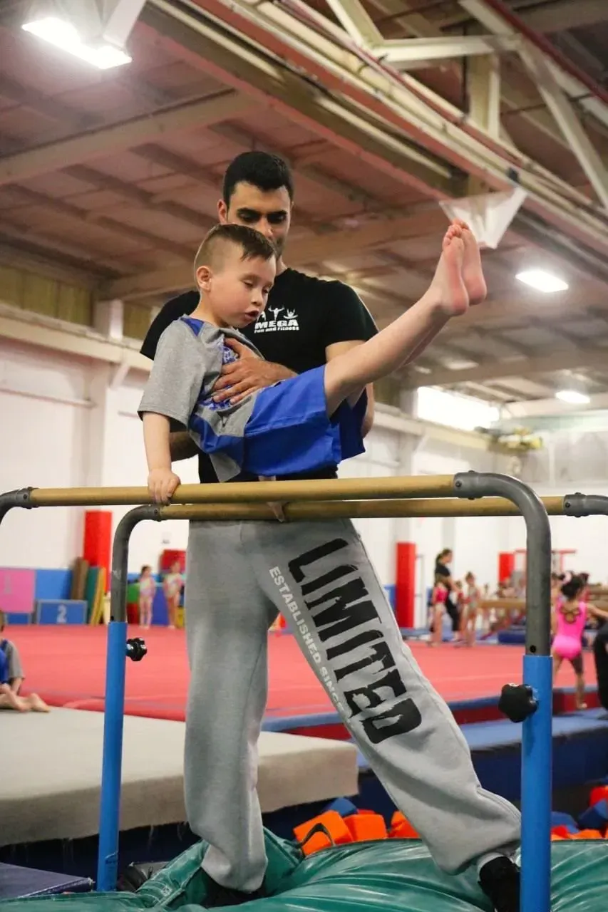 a man is helping a young boy do gymnastics on parallel bars