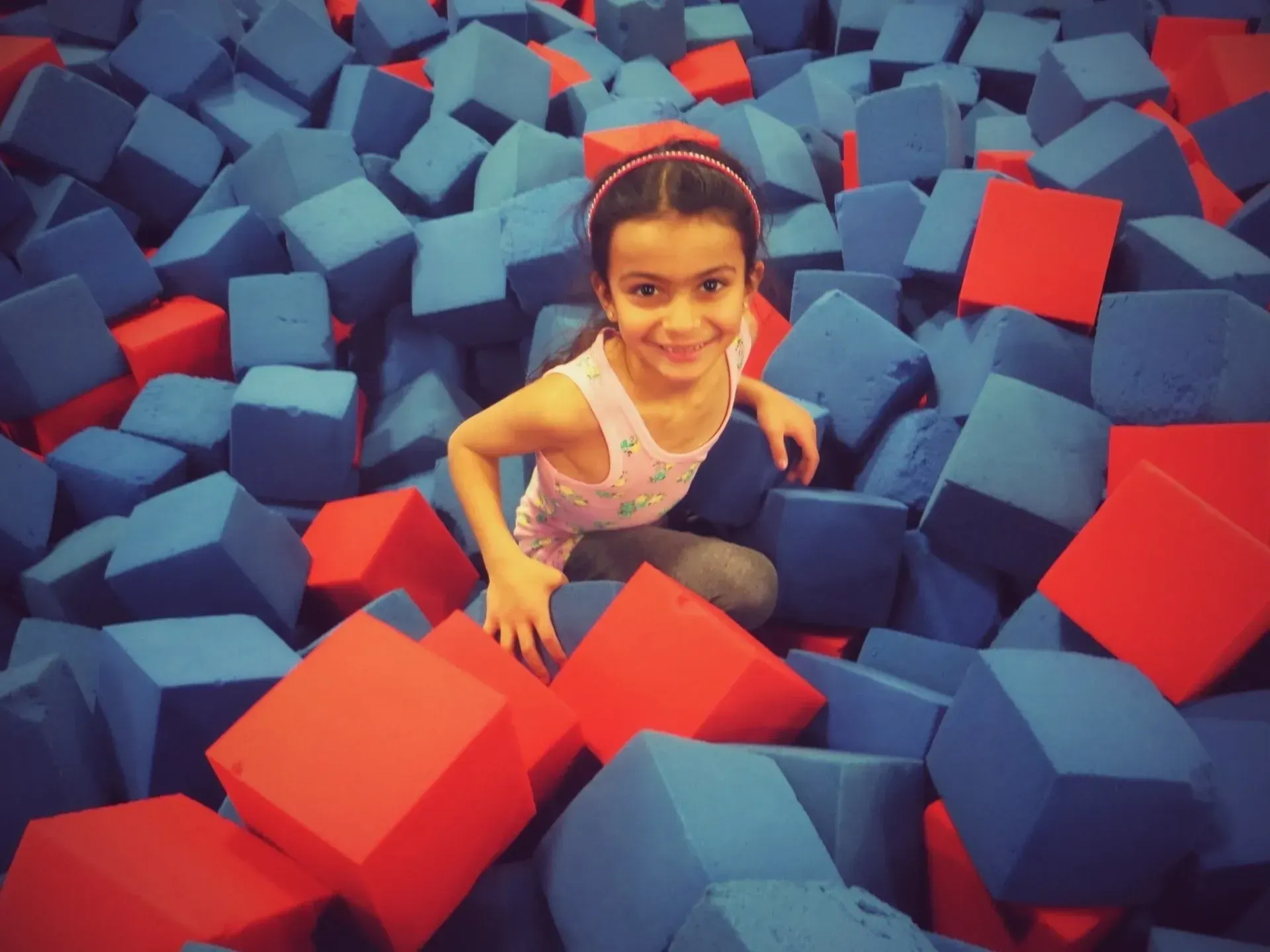 a little girl is sitting in a pile of blue and red foam cubes