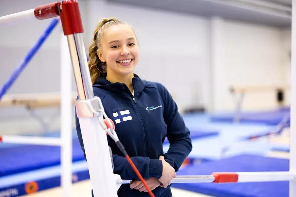 A young woman is standing next to a bar in a gym and smiling.