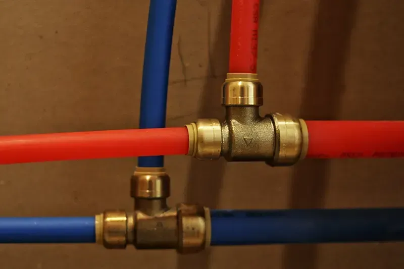 Blue and red PEX pipes connected with brass fittings, against a brown wall.