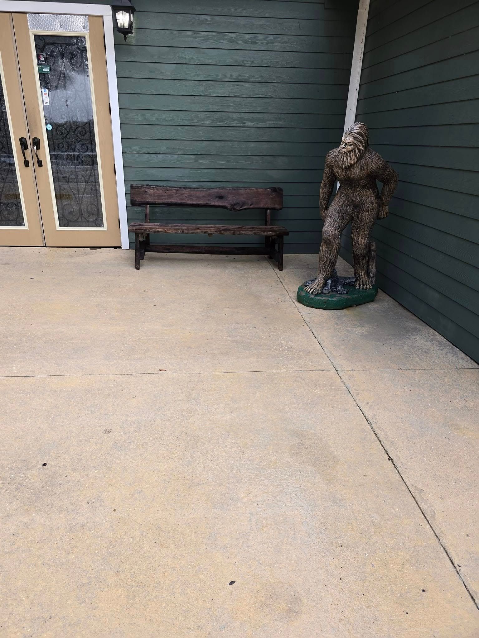 A statue of a soldier is standing next to a wooden bench.