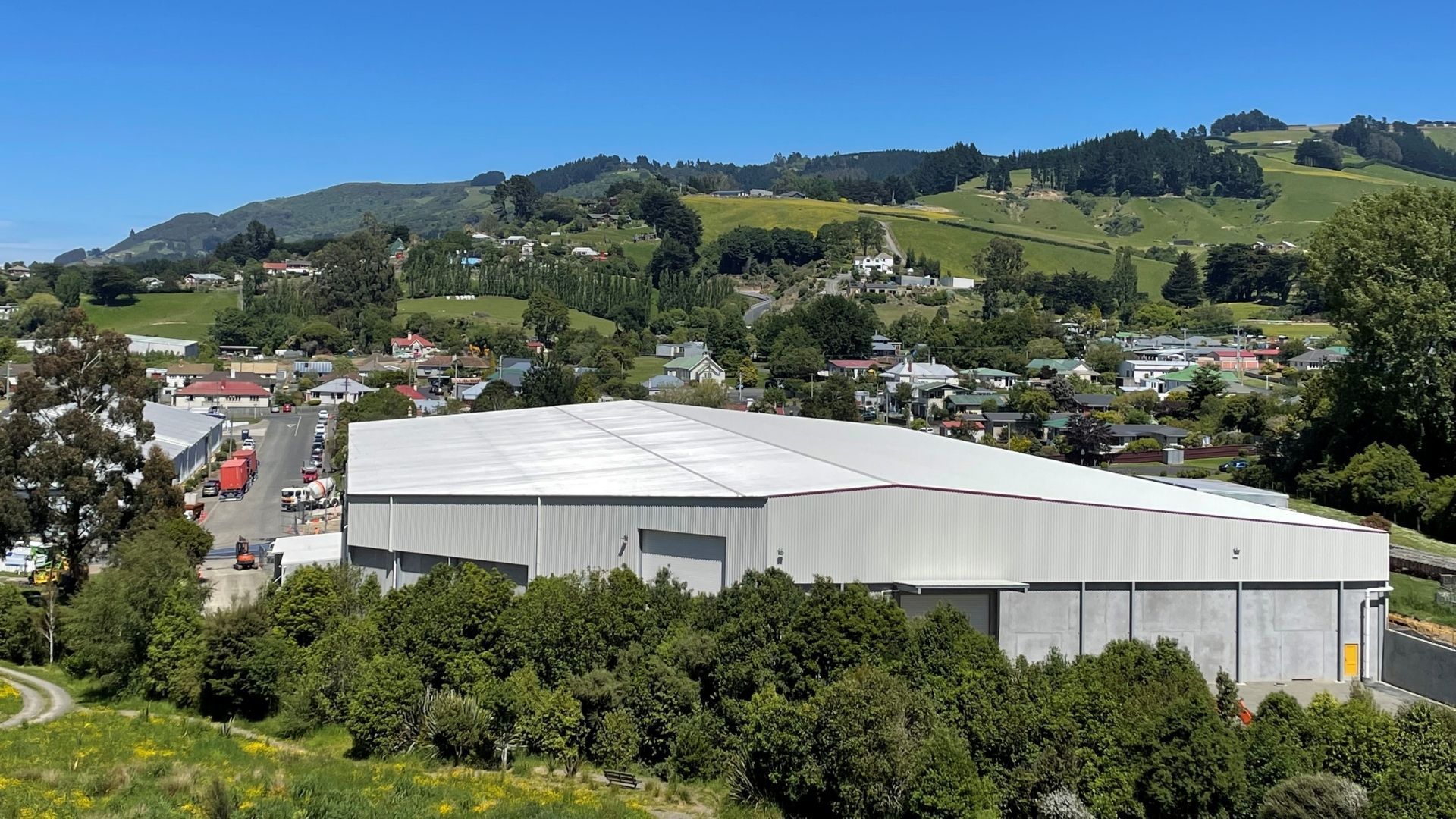 A large white building is surrounded by trees and mountains in the background.