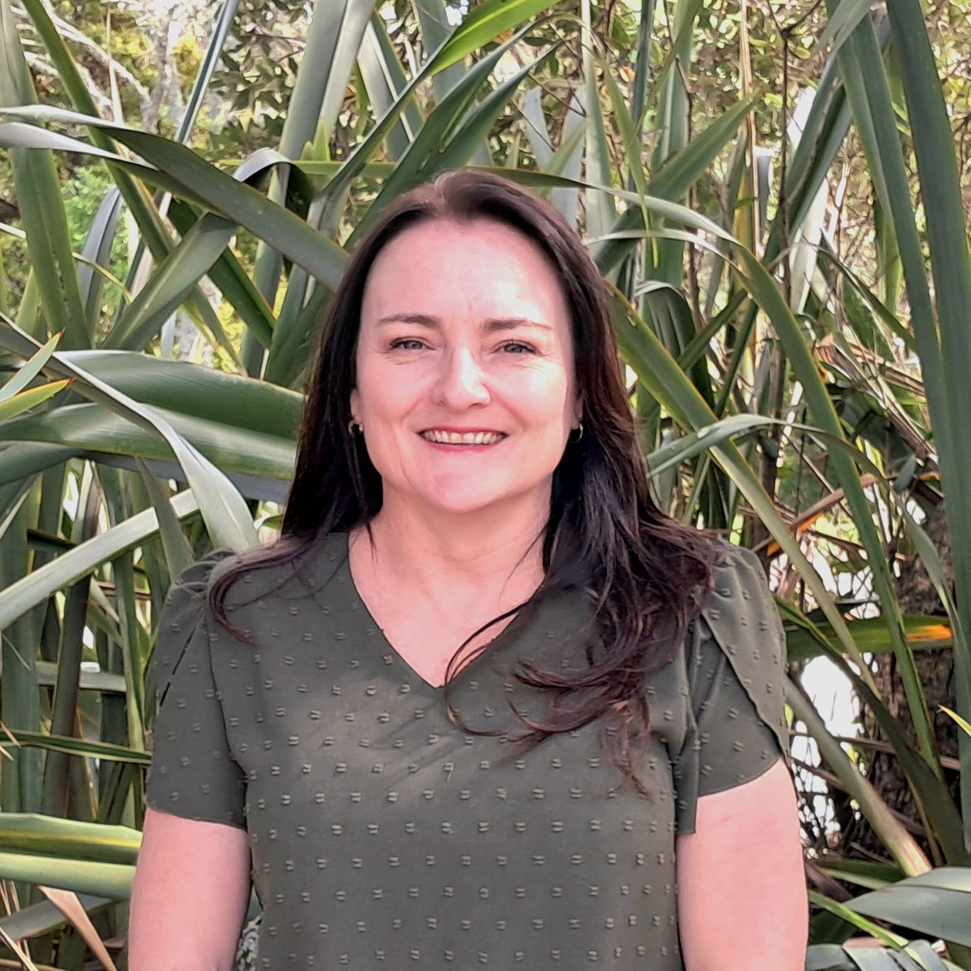A woman wearing glasses and a floral shirt is standing in front of trees.