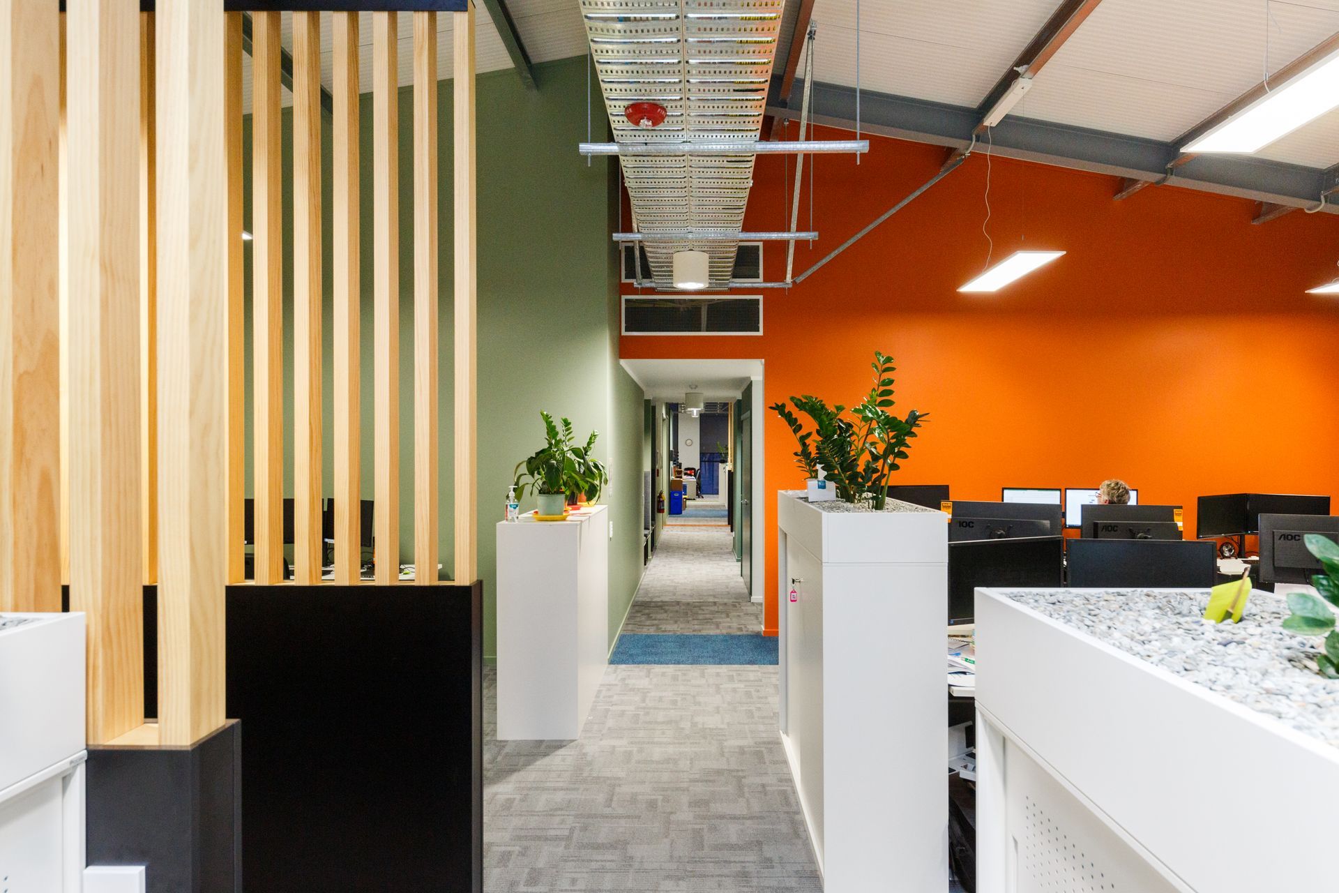 A hallway in an office with orange walls and desks.